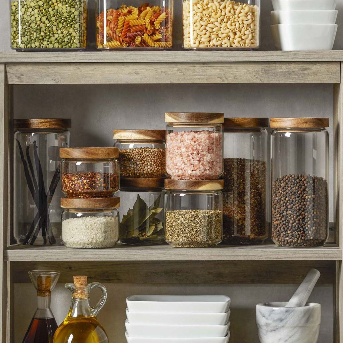 A person arranging prepared ingredients in glass containers on a wooden counter